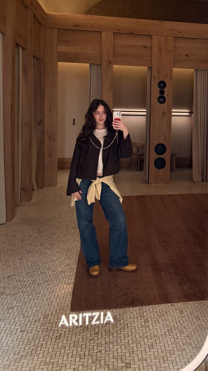 Cropped jacket over a white tee with a yellow sweater tied at the waist, wide-leg denim and tan loafers