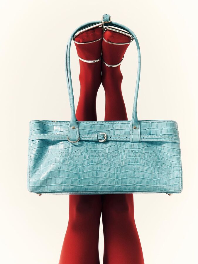 Turquoise croc bag hanging from legs in red tights