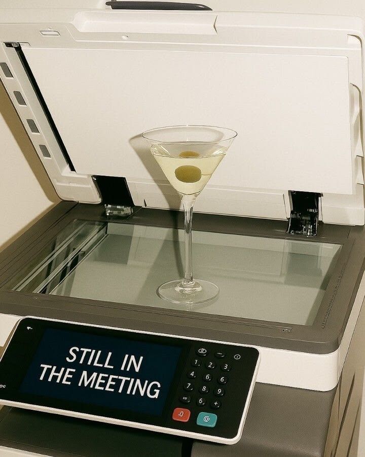 Martini glass on a copier whose screen reads Still in the meeting
