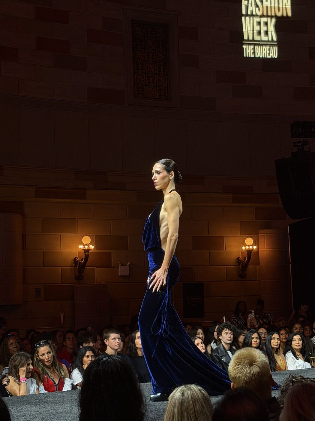 Model in a navy velvet gown at the end of the runway under The Bureau Fashion Week sign