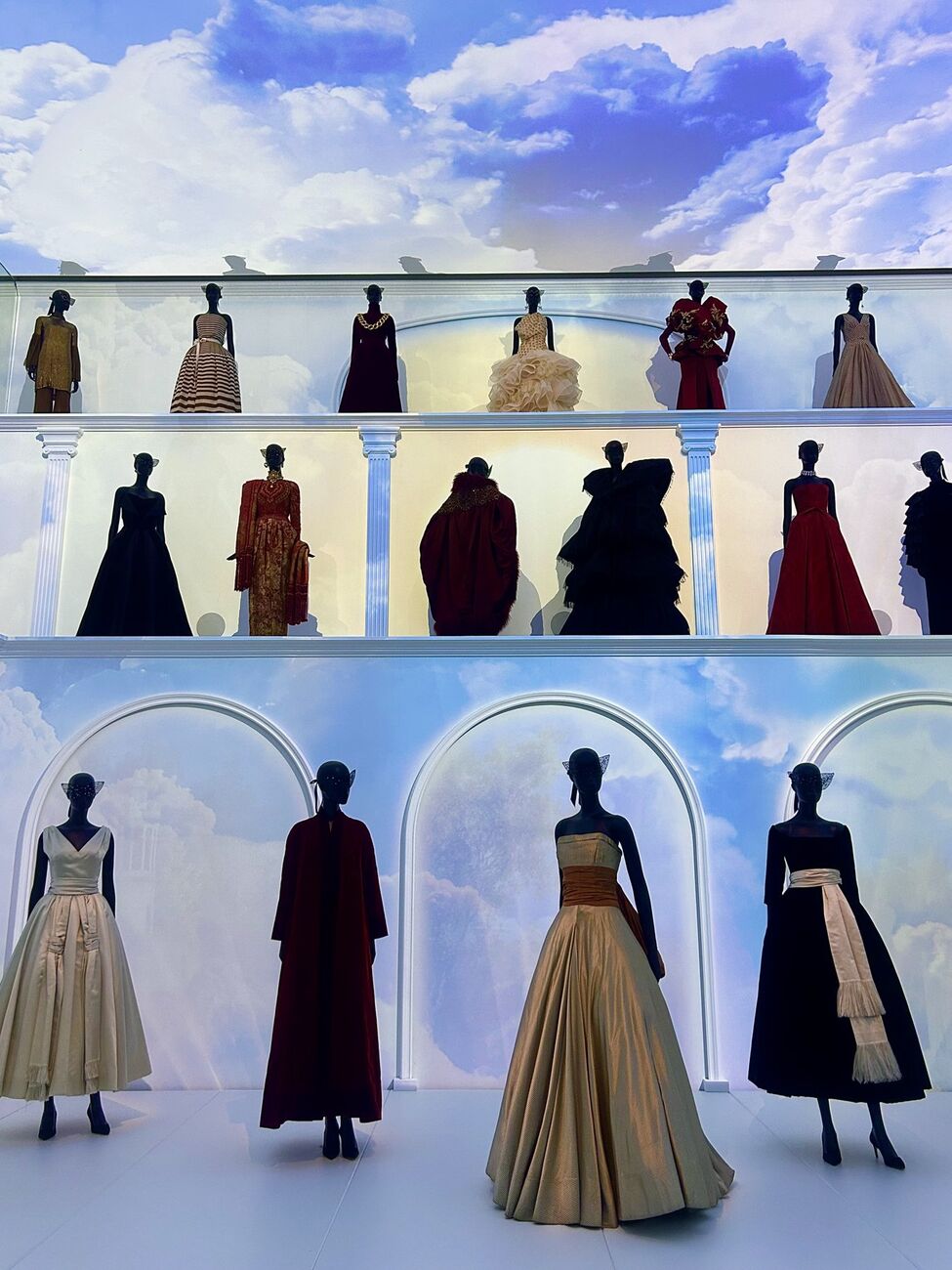 Rows of Dior couture gowns displayed against a painted sky