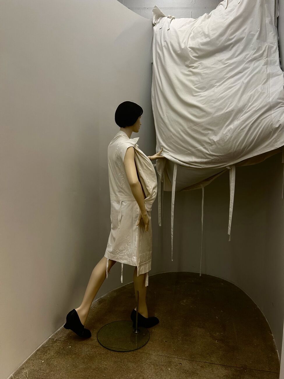 Mannequin in a white dress beside a draped canvas installation at Dover Street Market Paris