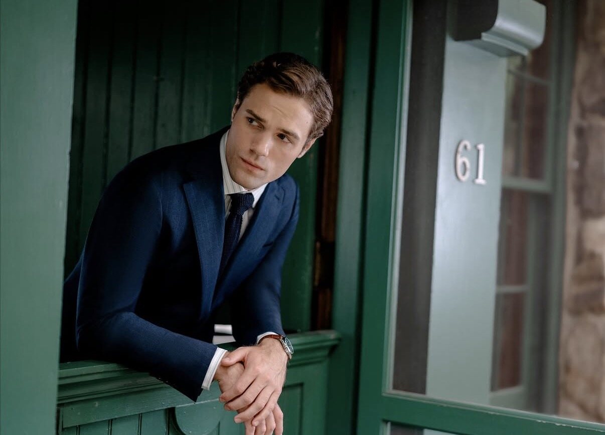 Hickey Freeman campaign image of a model in a navy pinstripe suit leaning out of a green cabin window