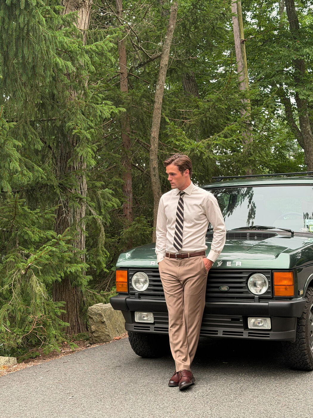 Model in khakis and tie leaning on a vintage Land Rover