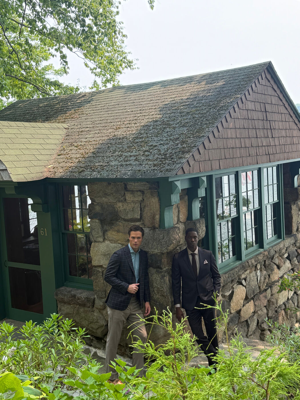 Two models in suits outside a stone lake house