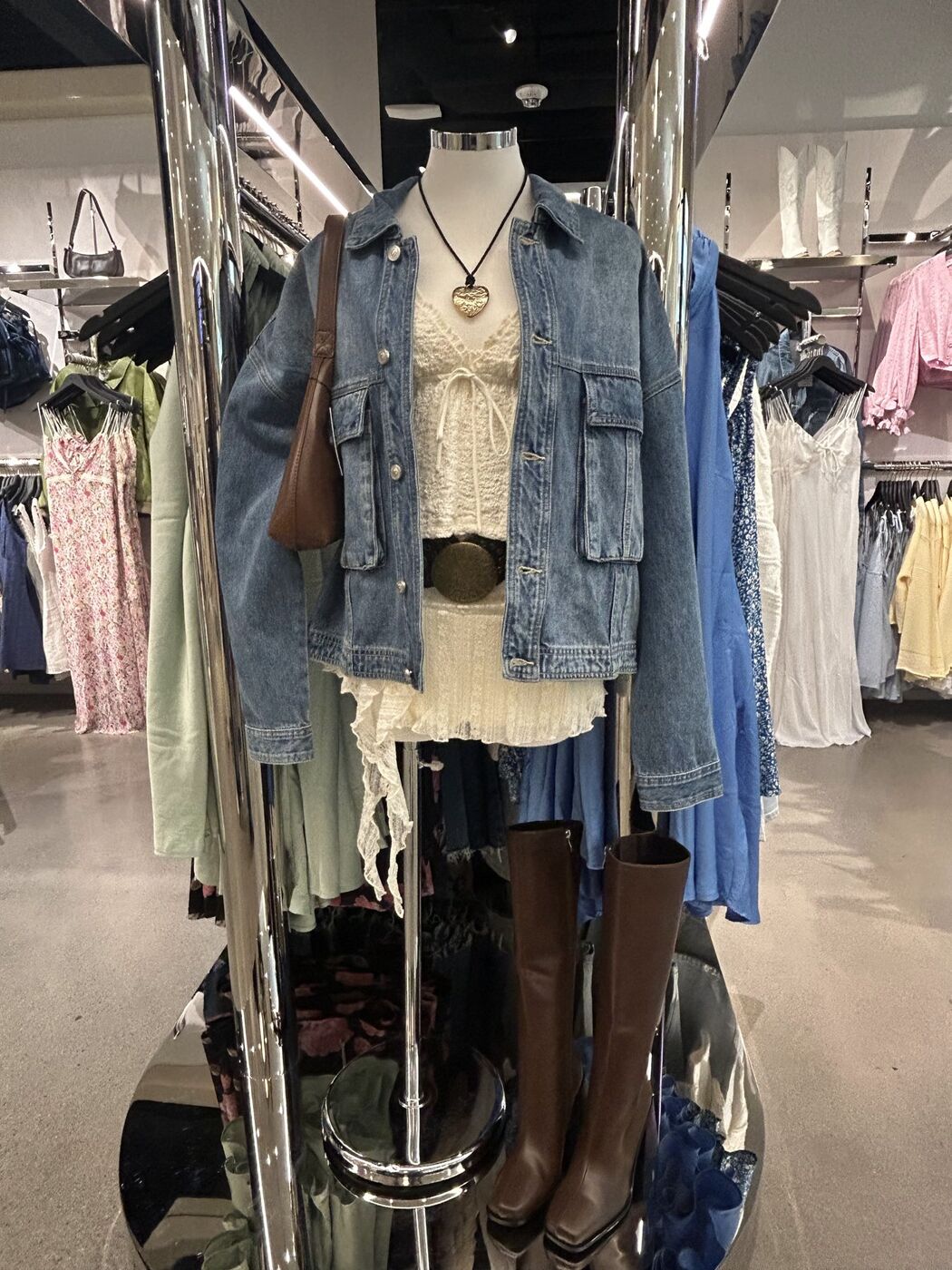 Mannequin in a denim jacket, lace top, belt and knee-high boots on a mirrored stand